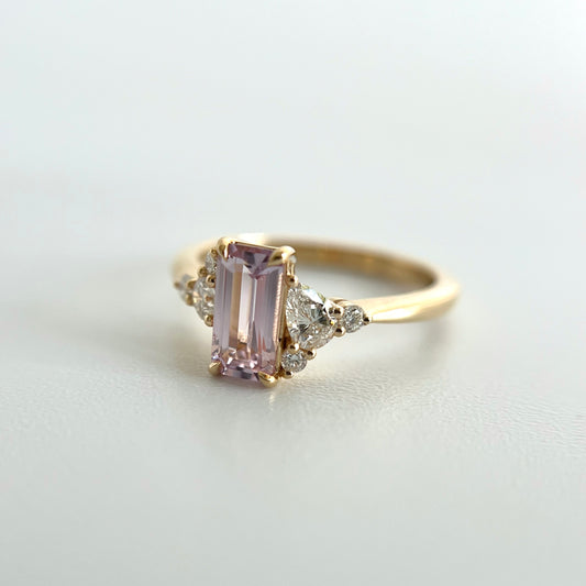 Angled view of a 14k yellow gold ring, eagle claw set with a light pink emerald-cut sapphire, and natural diamond accents. This photo puts an emphasis on the larger pear shape and two smaller round diamond accents on the right side of the ring.