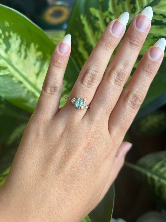 1.47ct unheated cushion cut green Montana sapphire and diamond cluster ring in 14k yellow gold, worn on hand showing stone colour and asymmetric diamond setting