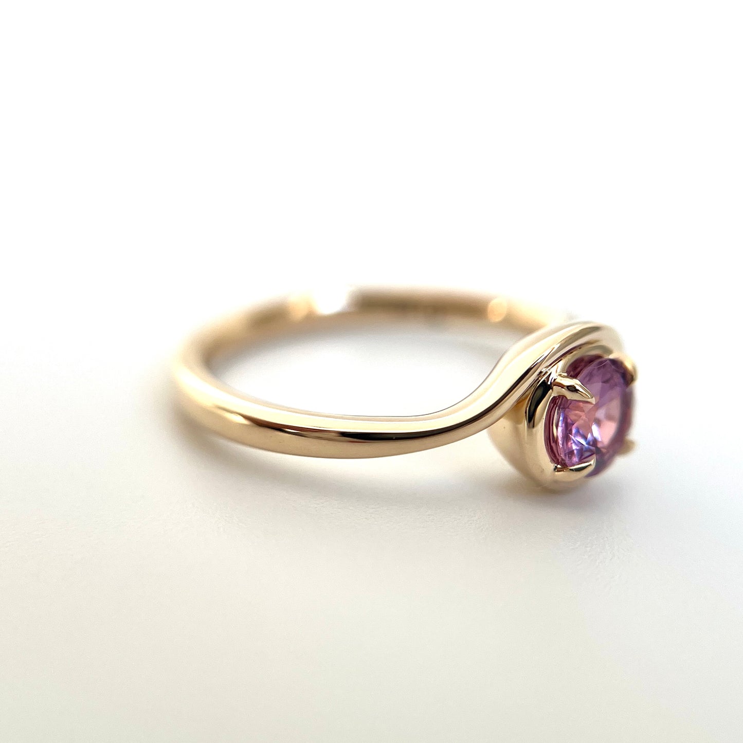Pink sapphire solitaire ring in 14k yellow gold, angled view showing wave band and setting detail
