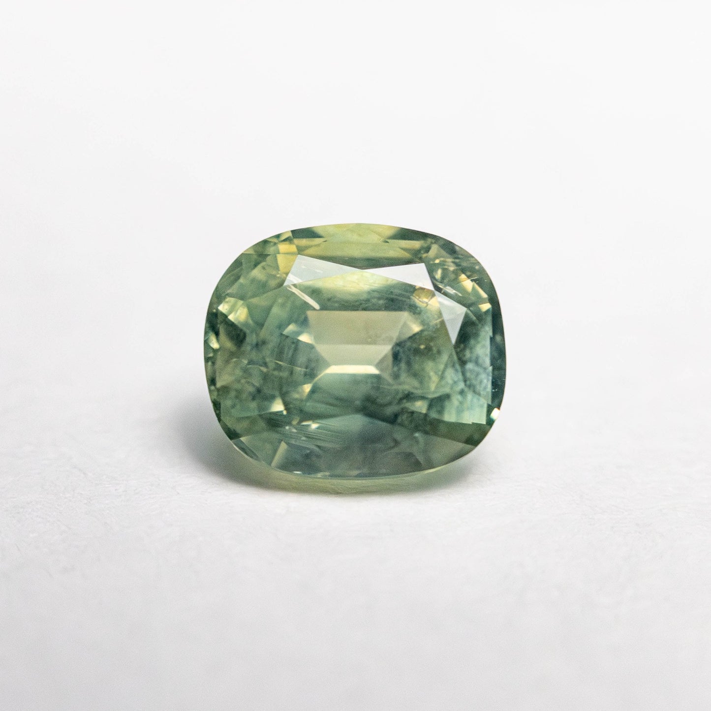 1.47ct unheated cushion cut green Montana sapphire, loose stone on white background showing colour and faceting