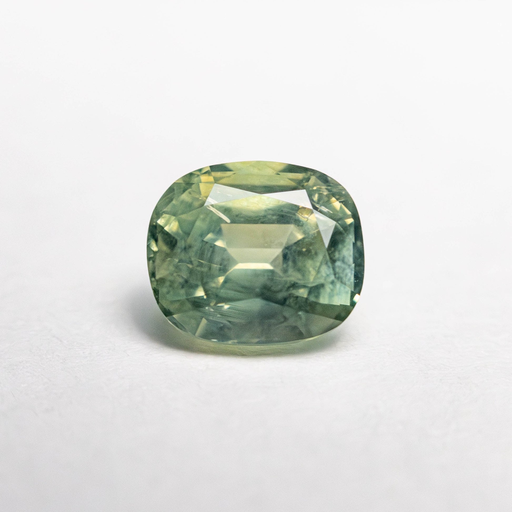 1.47ct unheated cushion cut green Montana sapphire, loose stone on white background showing colour and faceting