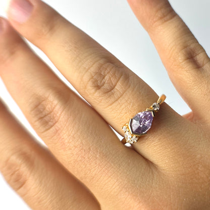 yellow gold ring with a purple sapphire and diamond accents on the east-west sides, on a person's ring finger
