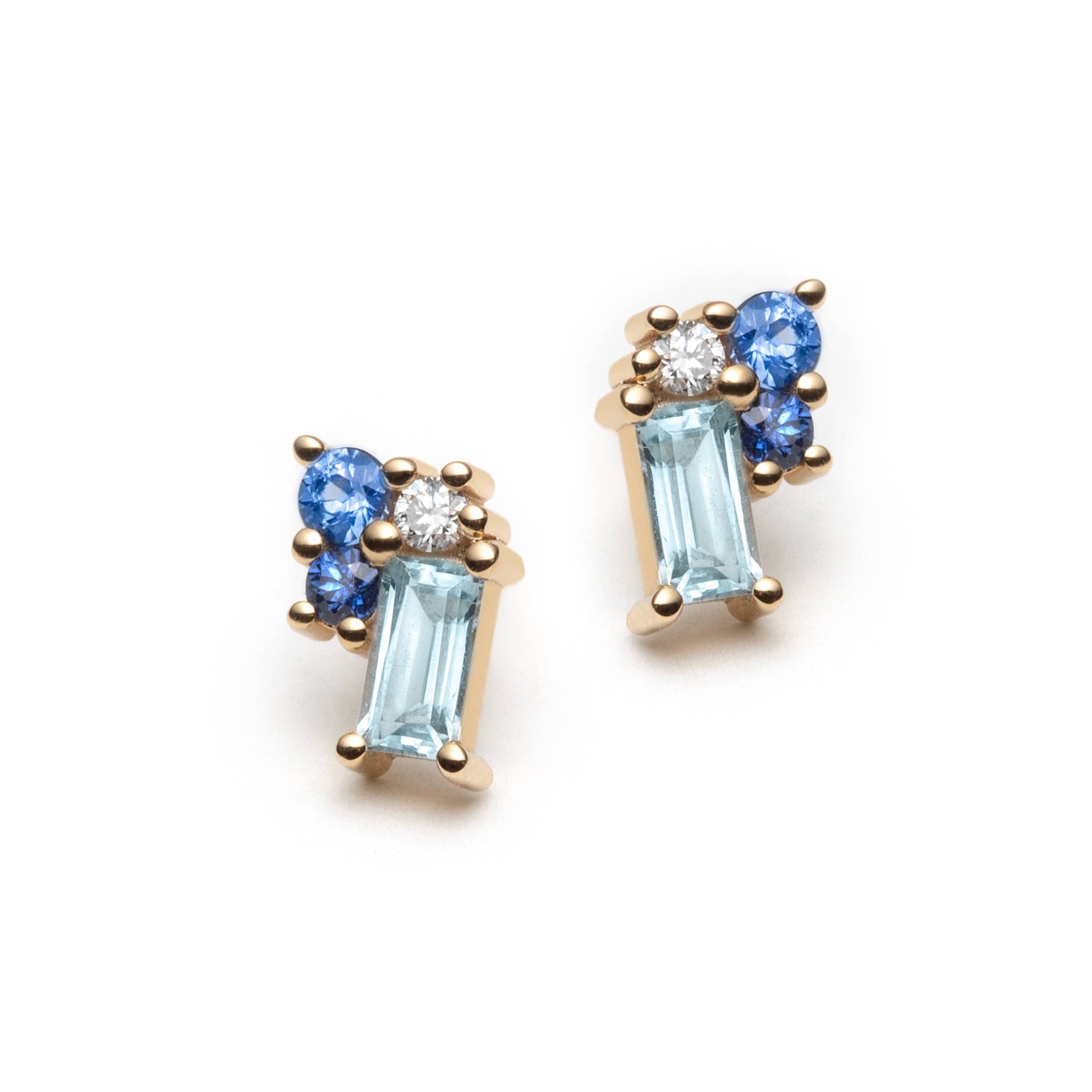 Blue gemstone clister stud earrings on a white background. The studs are set with baguette-cut blue topaz, 2 blue sapphires of different tones, and colorless diamonds. 