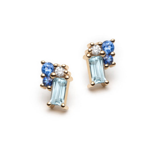 Blue gemstone clister stud earrings on a white background. The studs are set with baguette-cut blue topaz, 2 blue sapphires of different tones, and colorless diamonds. 
