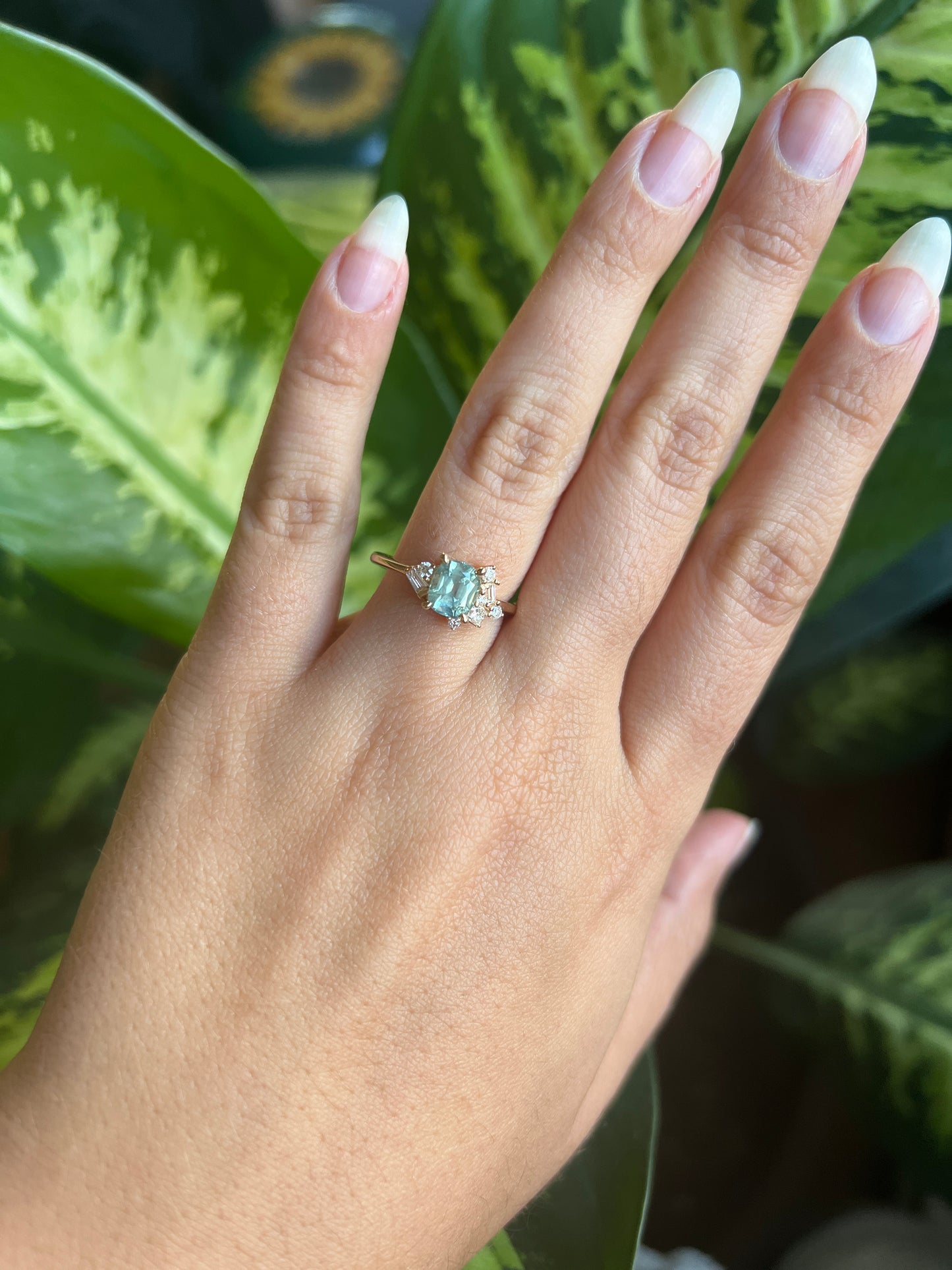 1.47ct unheated cushion cut green Montana sapphire and diamond cluster ring in 14k yellow gold, worn on hand showing stone colour and asymmetric diamond setting