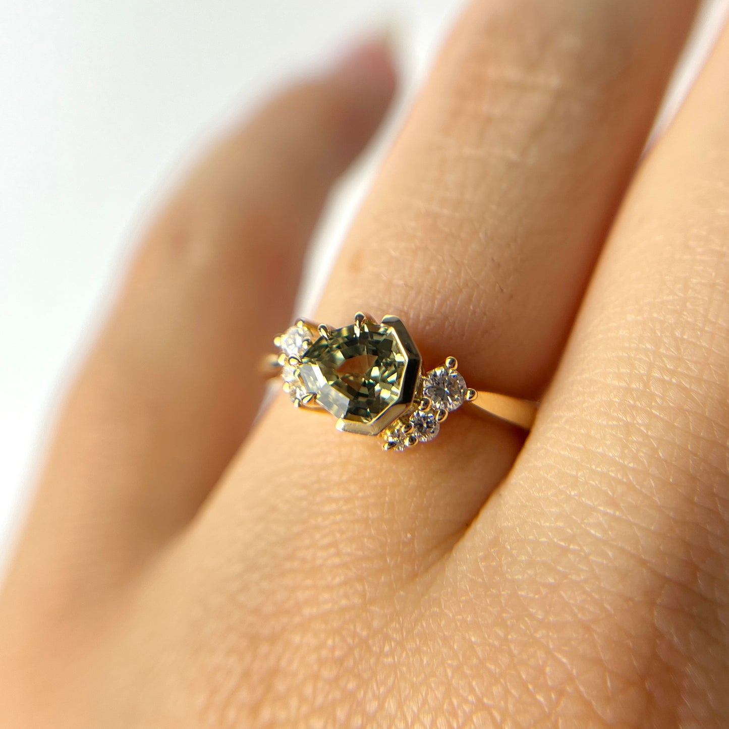 Close-up of 1.27ct unheated geometric trillion cut green Madagascar sapphire and diamond ring in 18k yellow gold, worn on hand showing stone colour and eagle claw half bezel setting