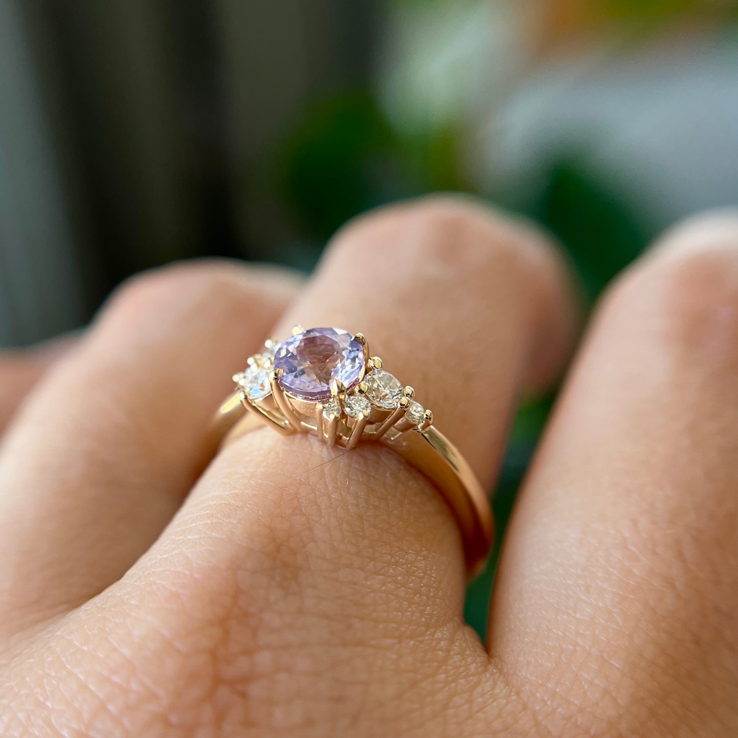 Gros plan de la bague de fiançailles en saphir violet clair et diamants en or jaune 14k, portée au doigt montrant la couleur lilas de la pierre et la hauteur du serti