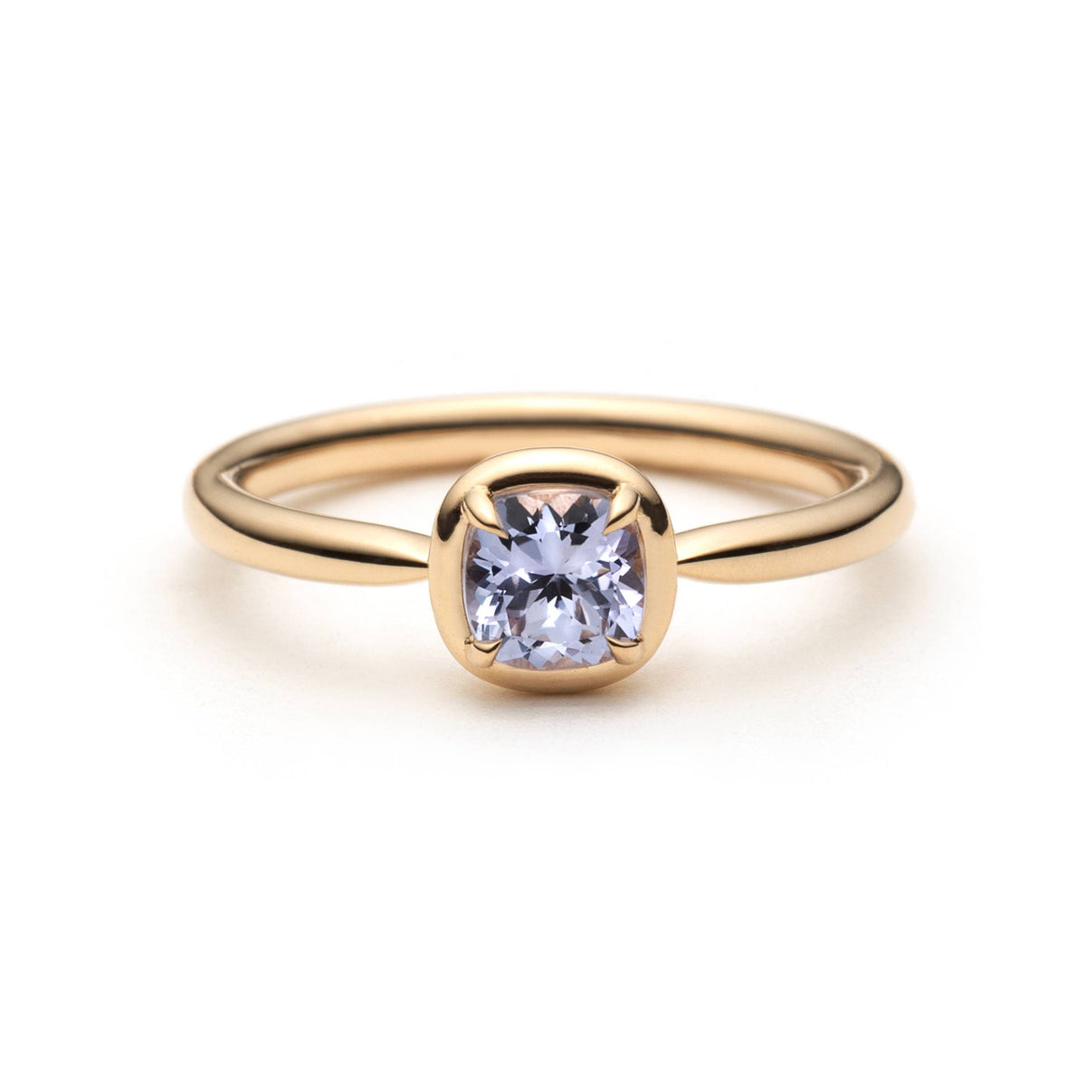 A gold ring with a cushion-cut light purple sapphire in a eagle-claw setting with a gold border. Shown on a clean white background.