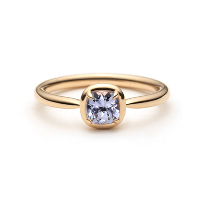 A gold ring with a cushion-cut light purple sapphire in a eagle-claw setting with a gold border. Shown on a clean white background.