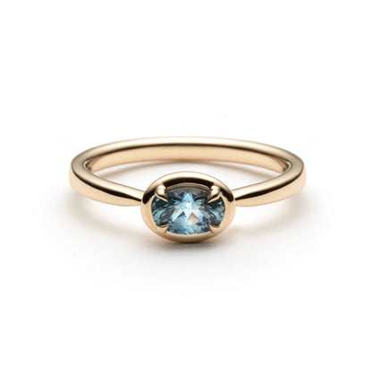 Denim blue oval montana sapphire set horizontally between 4 claws, in a frame bezel-like setting. The solitaire is shown on top of a white background. 
