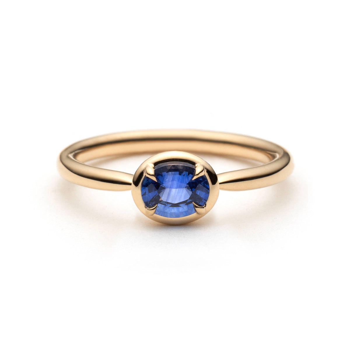 Gold solitaire ring with an oval blue sapphire, horizontally set in eagle-claws with a border of gold, placed on a clean white background