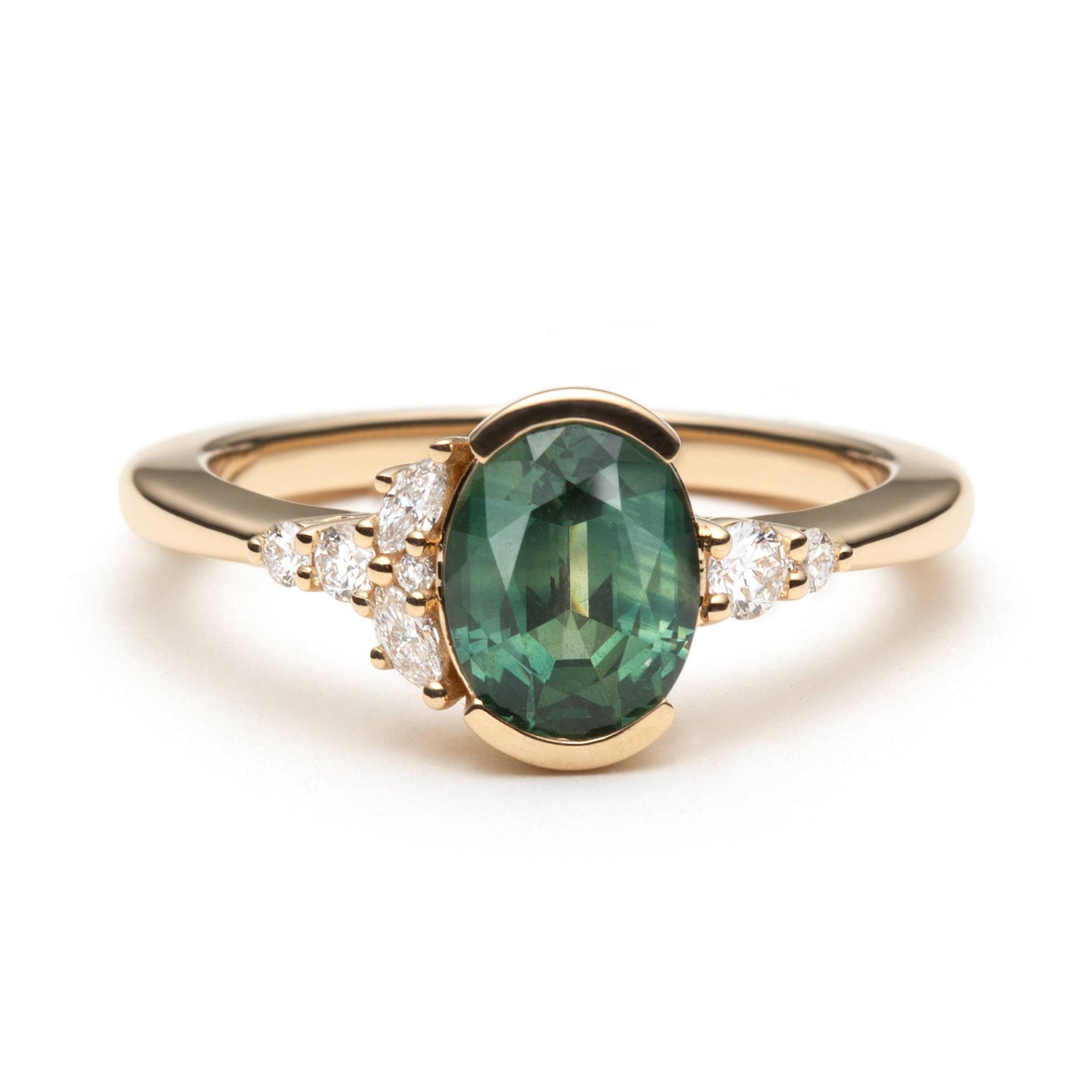 Oval green sapphire half-bezel set and accented by round brilliant cut and marquise shaped natural diamonds in an asymmetrical fashion. 