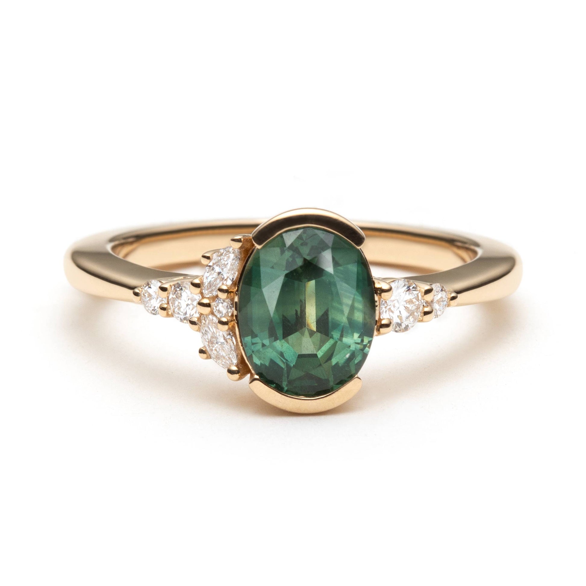 Oval green sapphire half-bezel set and accented by round brilliant cut and marquise shaped natural diamonds in an asymmetrical fashion. 