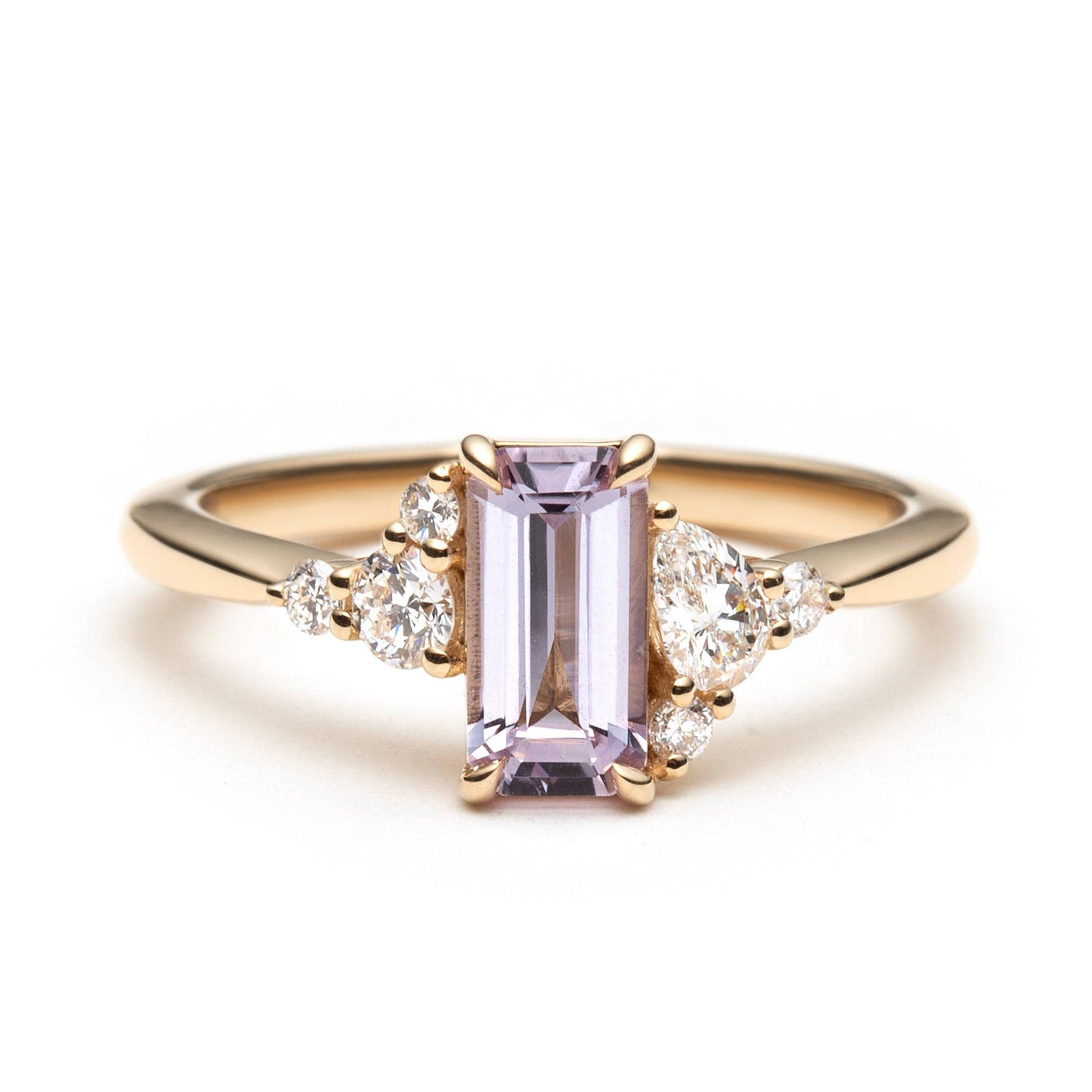 yellow gold ring with an emerald-cut pink sapphire and smaller natural diamonds set in an asymmetrical manner on a white background