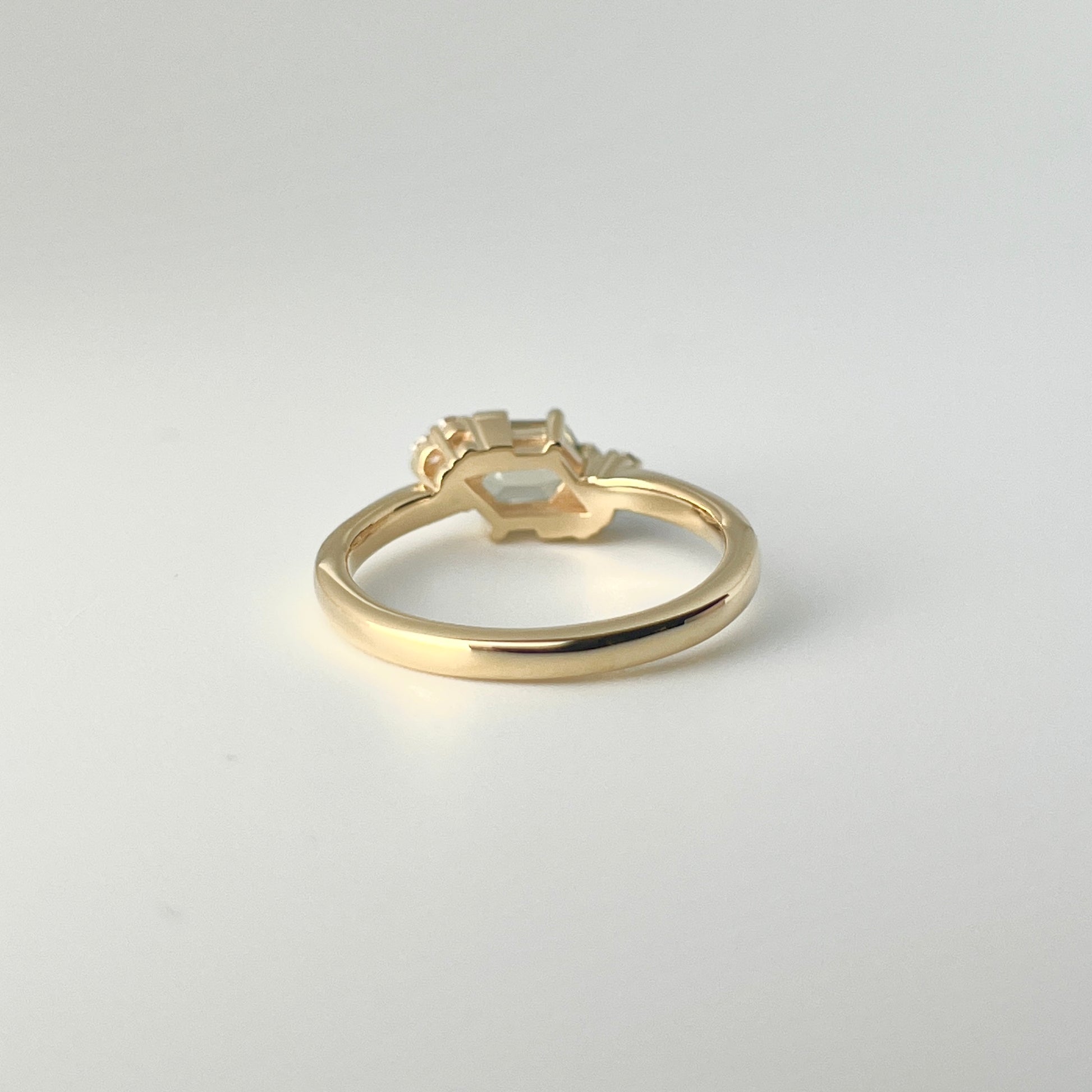 Underside view of yellow gold ring, showing diamond shaped opening to let the light through underneath a green sapphire