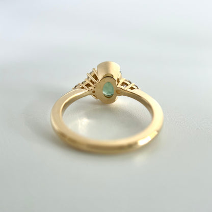 Under side view of a ring set with an oval green sapphire in the middle, with a half-bezel setting, and detailed view of the side open gallery settings for the small diamonds. 