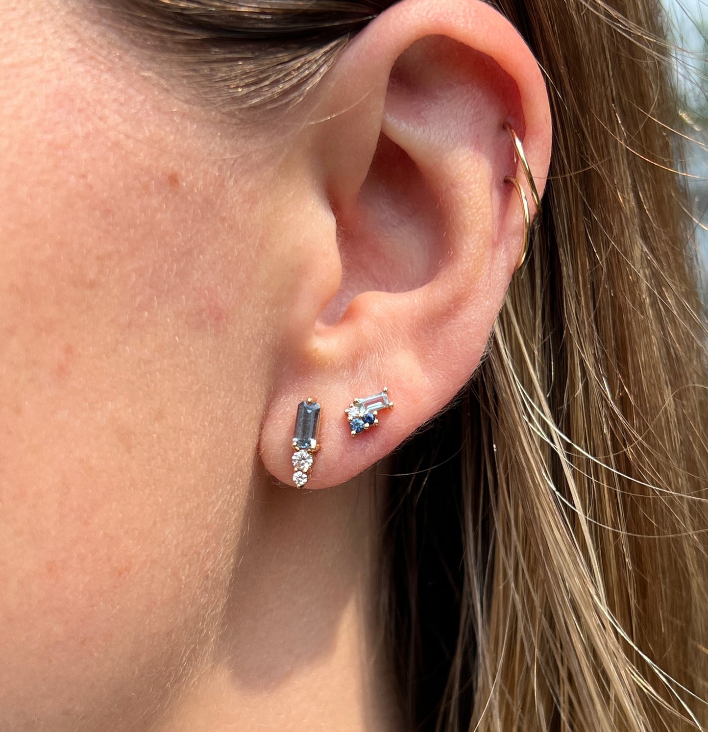 Two pairs of blue gemstone stud earrings worn side by side ear-lobes. 