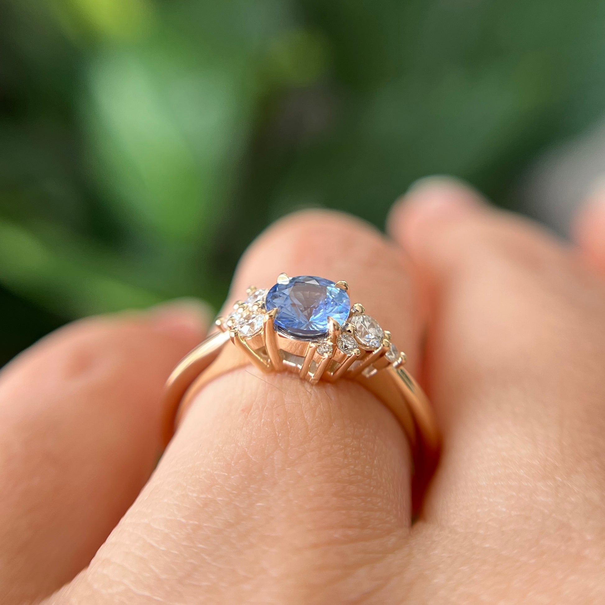 Gros plan de la bague de fiançailles en saphir bleu cornflower et diamants en or jaune 14k, portée au doigt montrant la couleur bleue de la pierre et la hauteur du serti