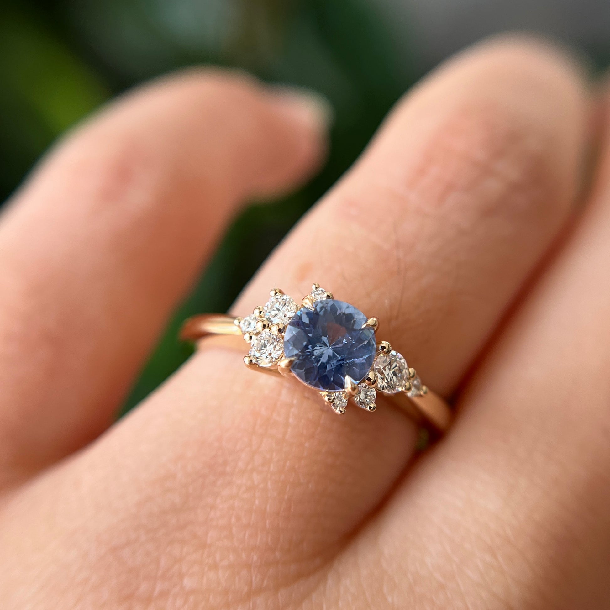 Bague de fiançailles en saphir bleu cornflower et diamants en or jaune 14k, portée au doigt montrant la couleur de la pierre et le détail des diamants