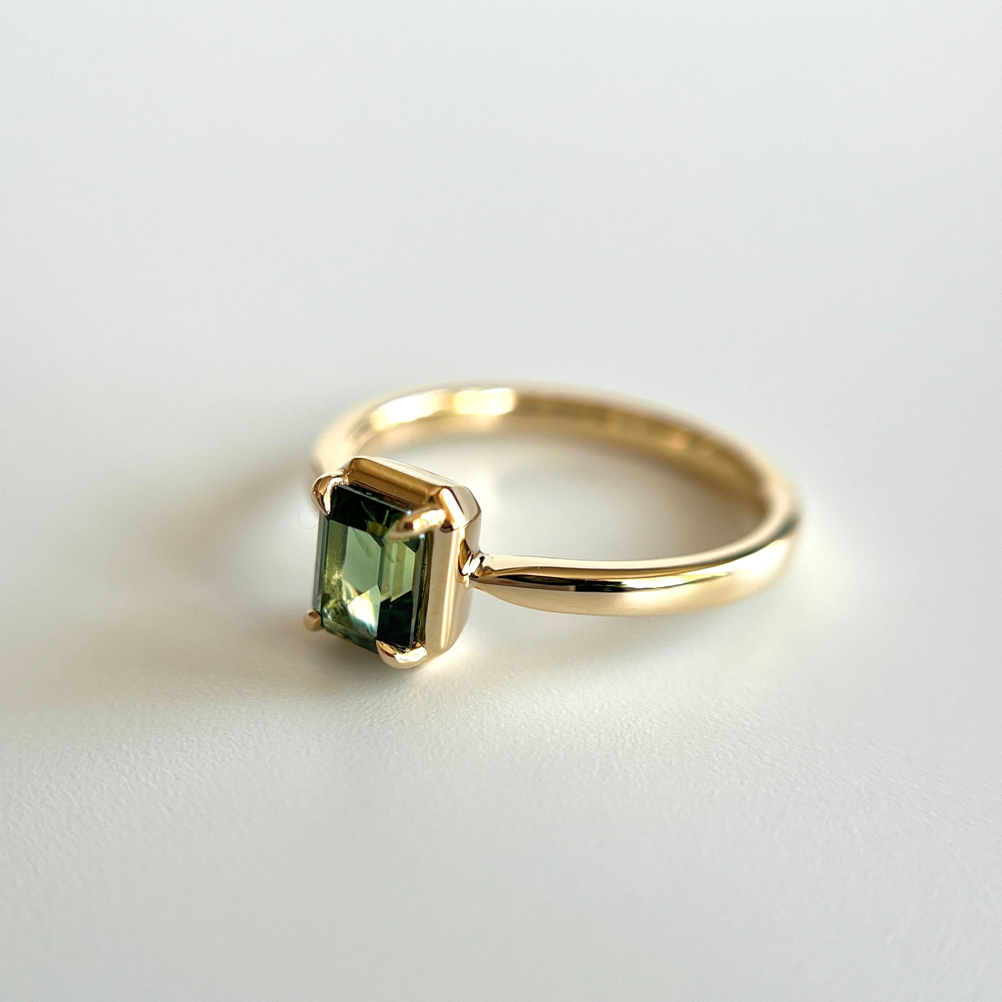 Bague de fiançailles solitaire en saphir vert forêt taille émeraude de 1,05ct de Madagascar en or jaune 14k, vue en angle montrant le détail du serti en griffes à cadre en or