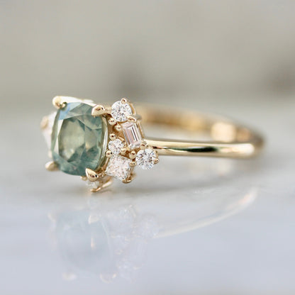 1.47ct unheated cushion cut green Montana sapphire and diamond cluster ring in 14k yellow gold, angled view showing stone colour and asymmetric diamond setting detail