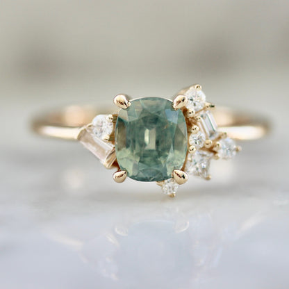1.47ct unheated cushion cut green Montana sapphire and diamond cluster ring in 14k yellow gold, close-up view showing stone colour and asymmetric baguette and round diamond setting
