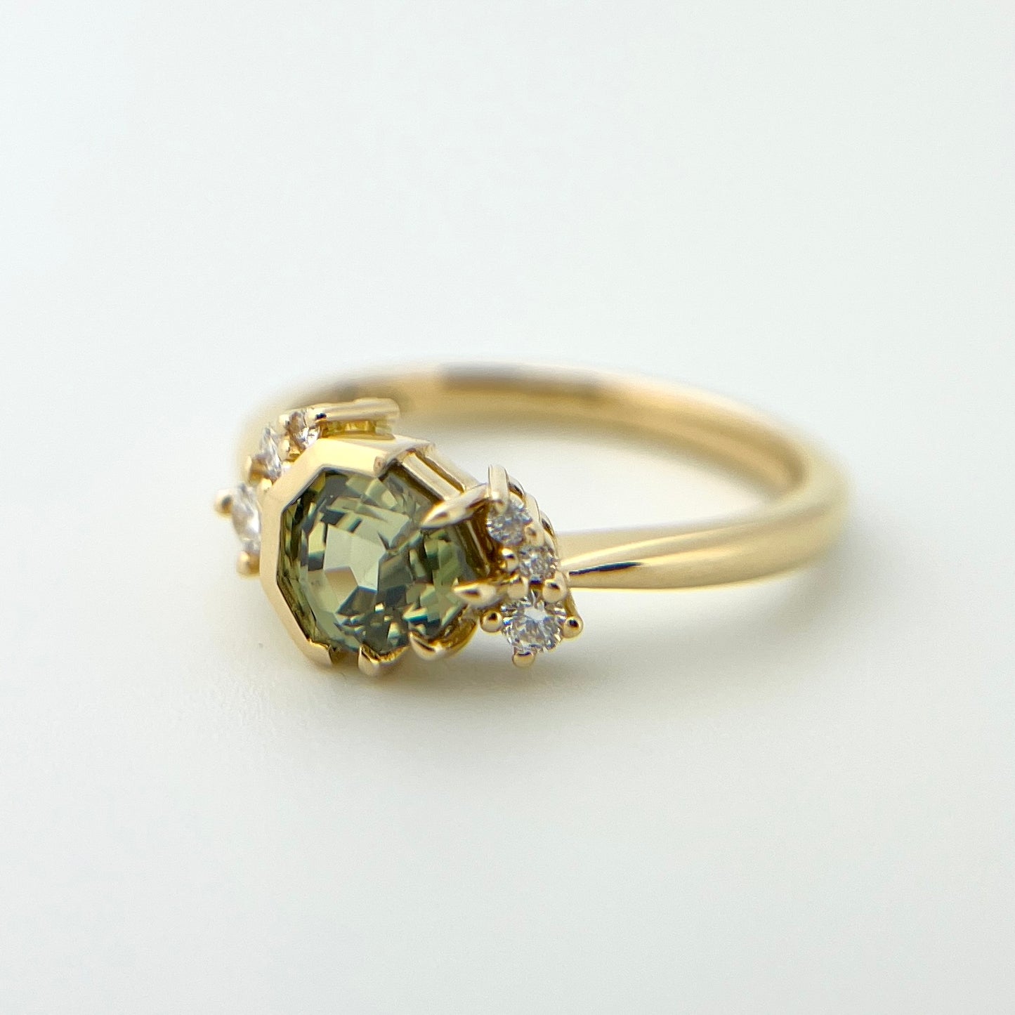 1.27ct unheated geometric trillion cut green Madagascar sapphire and diamond ring in 18k yellow gold, angled view showing eagle claw half bezel setting and band detail