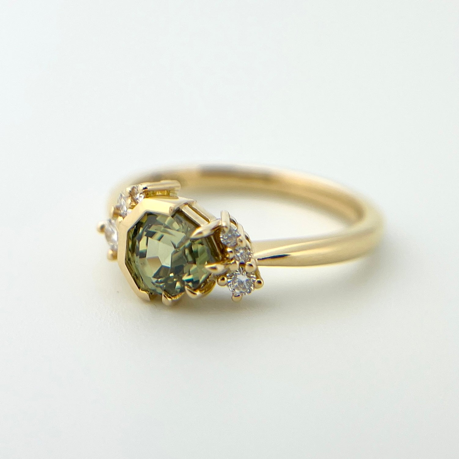 1.27ct unheated geometric trillion cut green Madagascar sapphire and diamond ring in 18k yellow gold, angled view showing eagle claw half bezel setting and band detail