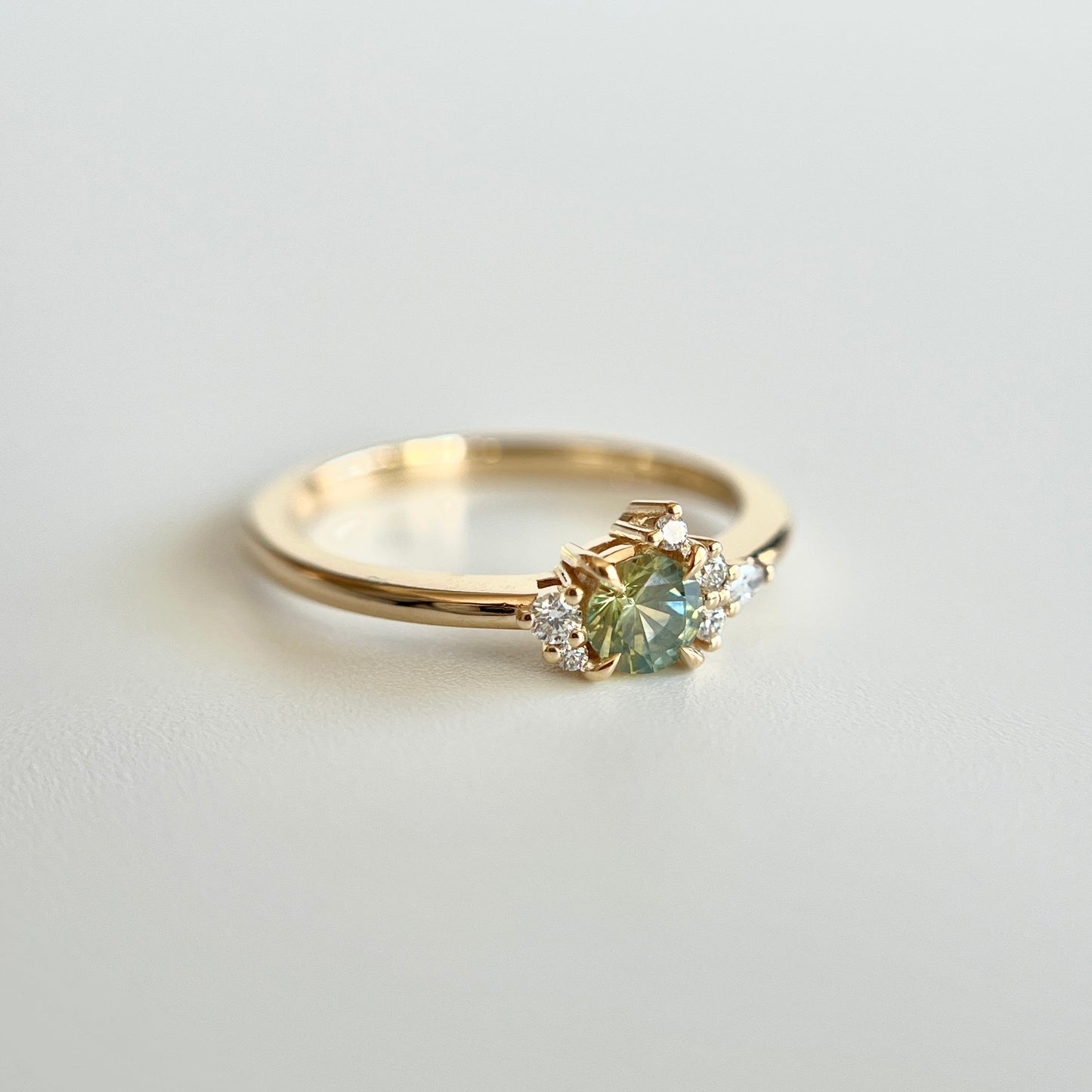 Bague de fiançailles en saphir bicolore rond de 0,36ct passant du jaune au bleu et diamants naturels en or jaune 14k, vue en angle montrant le changement de couleur de la pierre et le détail du cluster asymétrique
