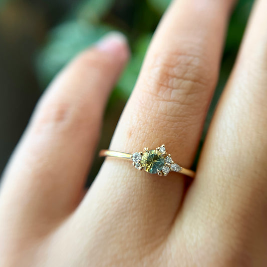 Bague de fiançailles en saphir bicolore rond de 0,36ct passant du jaune au bleu et diamants naturels en or jaune 14k, portée au doigt montrant le changement de couleur de la pierre et le cluster asymétrique