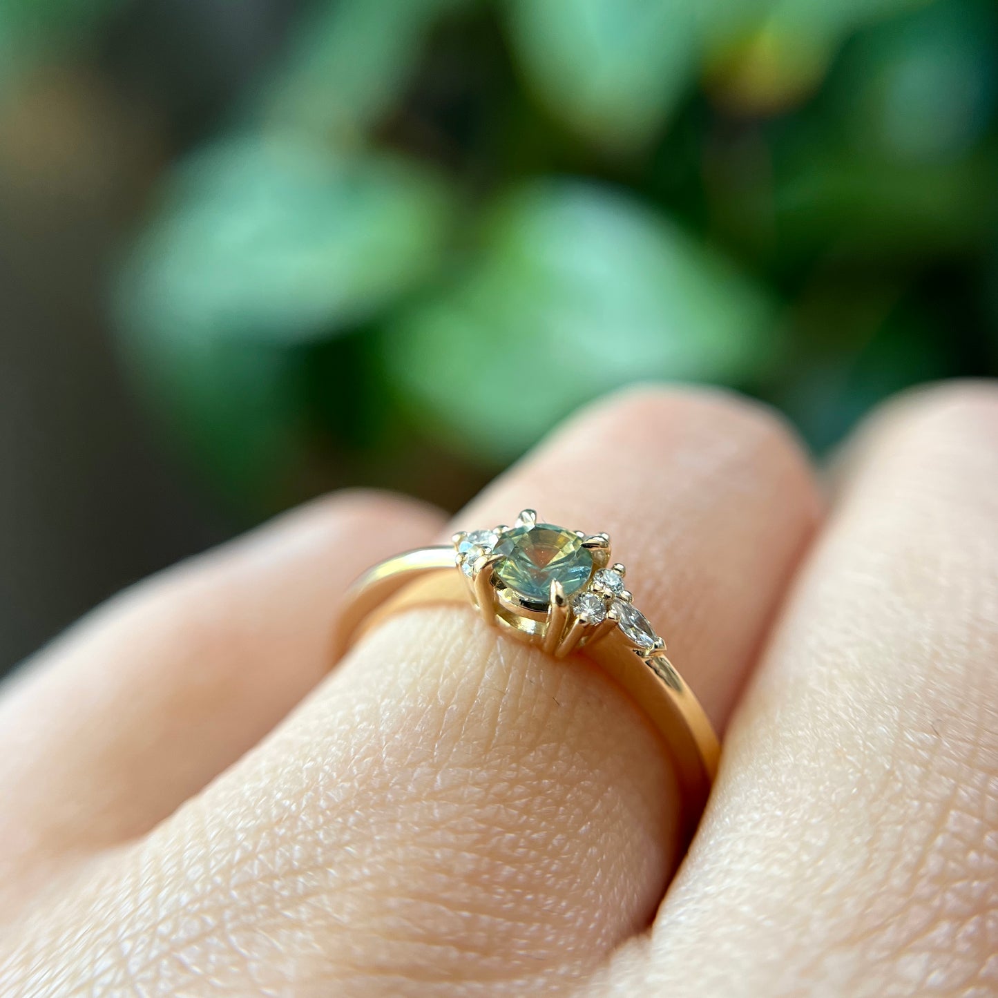 Bague de fiançailles en saphir bicolore rond de 0,36ct passant du jaune au bleu et diamants naturels en or jaune 14k, vue de côté portée au doigt montrant le profil du corps de bague et le changement de couleur de la pierre