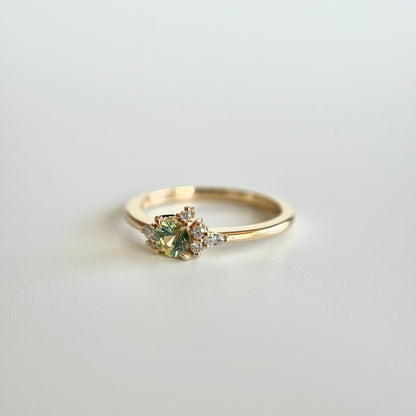 Bague de fiançailles en saphir bicolore rond de 0,36ct passant du jaune au bleu et diamants naturels en or jaune 14k, vue en trois-quarts montrant le changement de couleur de la pierre et le détail du cluster asymétrique
