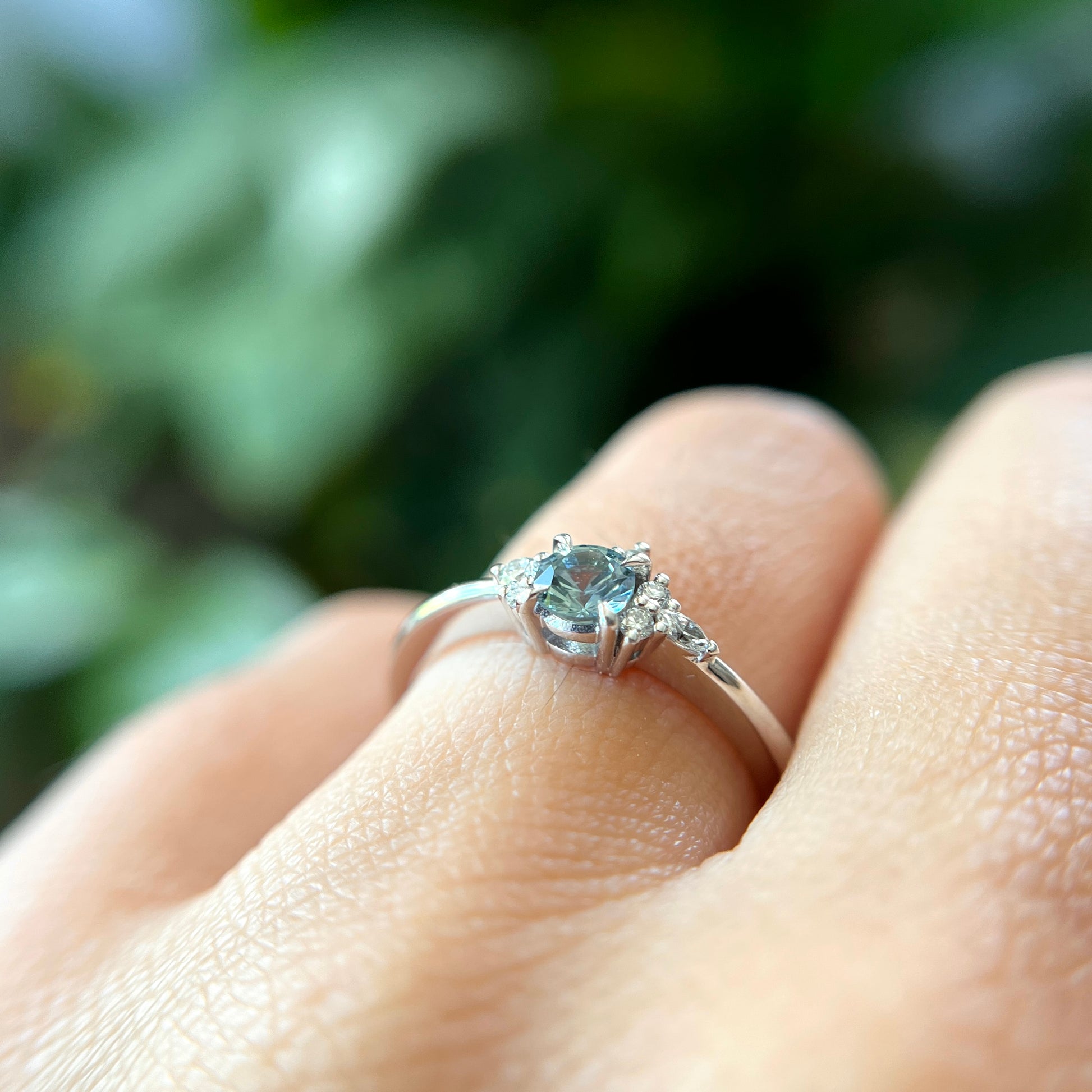 Bague de fiançailles en saphir bleu rond de 0,35ct et diamants naturels en or blanc 14k, vue de côté portée au doigt montrant le profil du corps de bague et la hauteur du serti