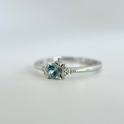 Bague de fiançailles en saphir bleu rond de 0,35ct et diamants naturels en or blanc 14k, vue en trois-quarts montrant la couleur de la pierre et le détail du cluster asymétrique