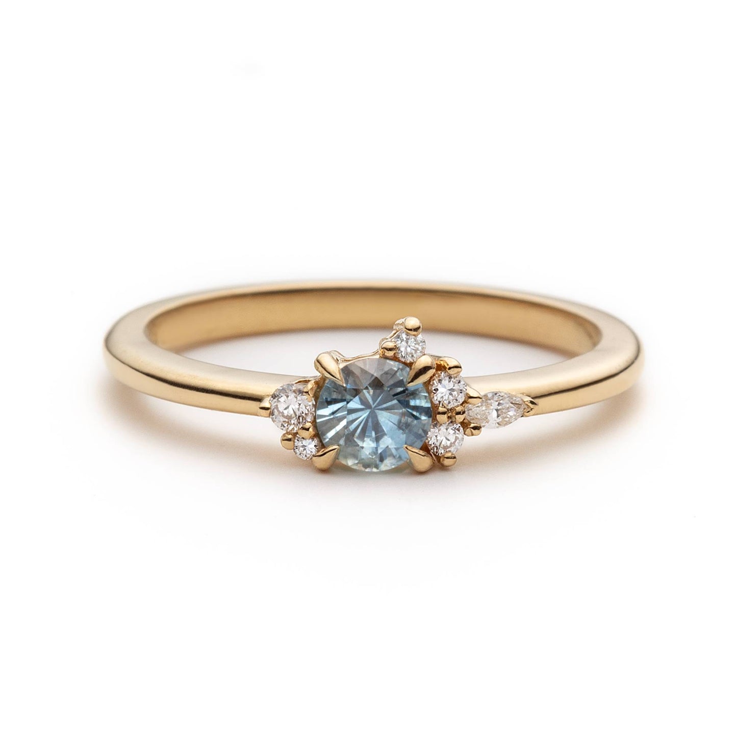 Bague de fiançailles en saphir bleu-sarcelle rond de 0,39ct et diamants naturels en or jaune 14k, vue de face sur fond blanc montrant la couleur de la pierre et le cluster asymétrique
