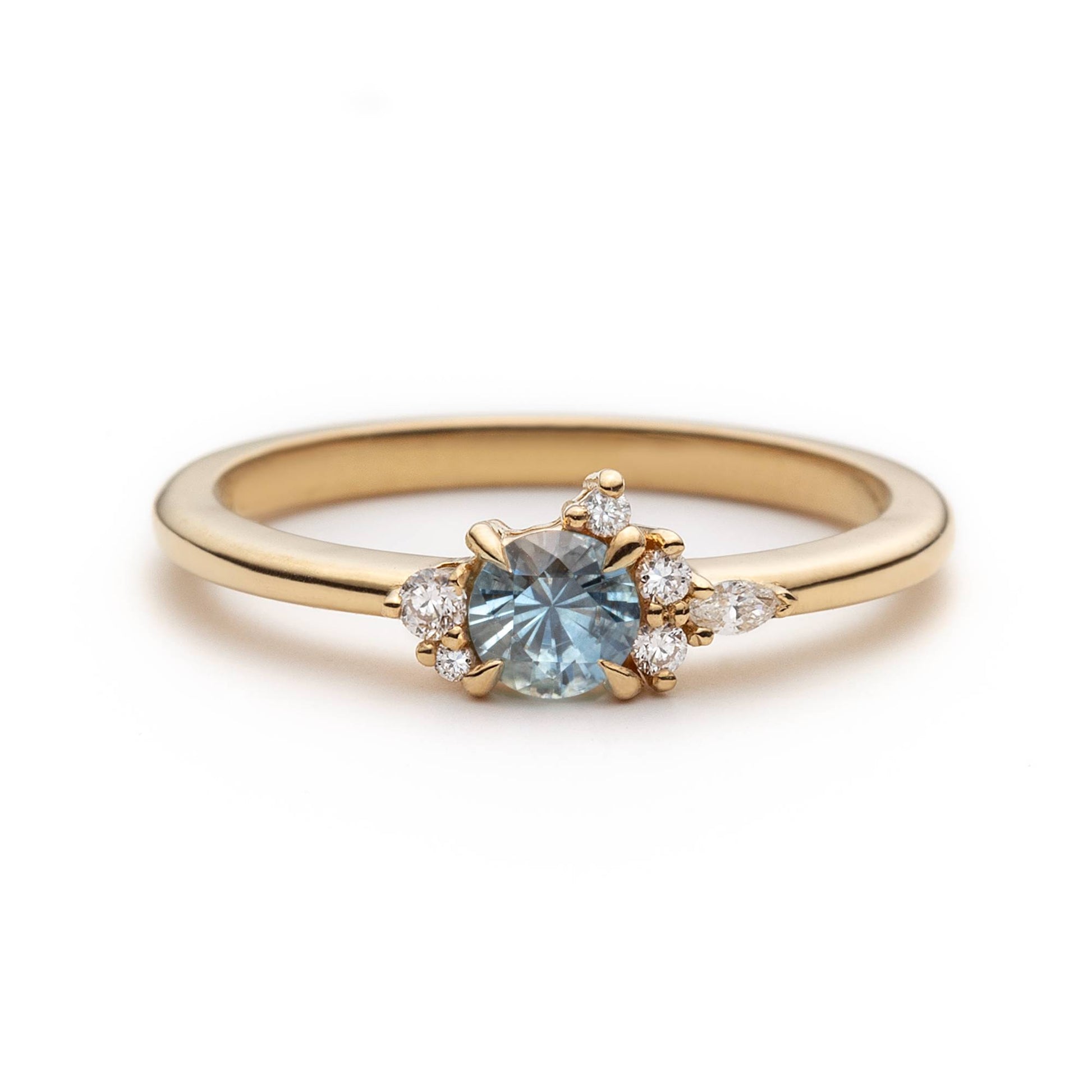 Bague de fiançailles en saphir bleu-sarcelle rond de 0,39ct et diamants naturels en or jaune 14k, vue de face sur fond blanc montrant la couleur de la pierre et le cluster asymétrique