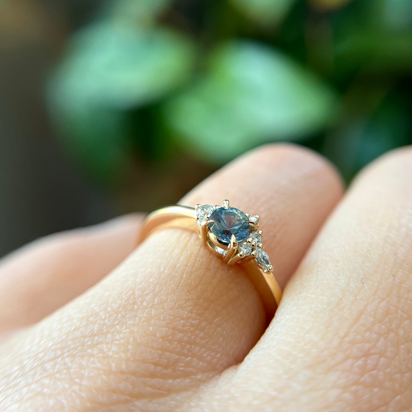 Bague de fiançailles en saphir bleu-sarcelle rond de 0,39ct et diamants naturels en or jaune 14k, vue de côté portée au doigt montrant le profil du corps de bague et la hauteur du serti