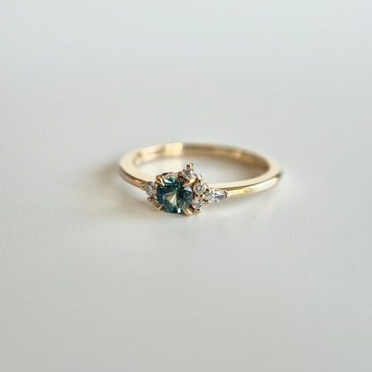 Bague de fiançailles en saphir sarcelle rond de 0,38ct et diamants naturels en or jaune 14k, vue en angle montrant le cluster asymétrique et le détail du corps de bague