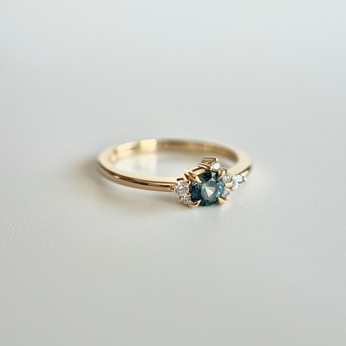 Bague de fiançailles en saphir sarcelle rond de 0,38ct et diamants naturels en or jaune 14k, vue en trois-quarts montrant la couleur de la pierre et le détail du cluster asymétrique