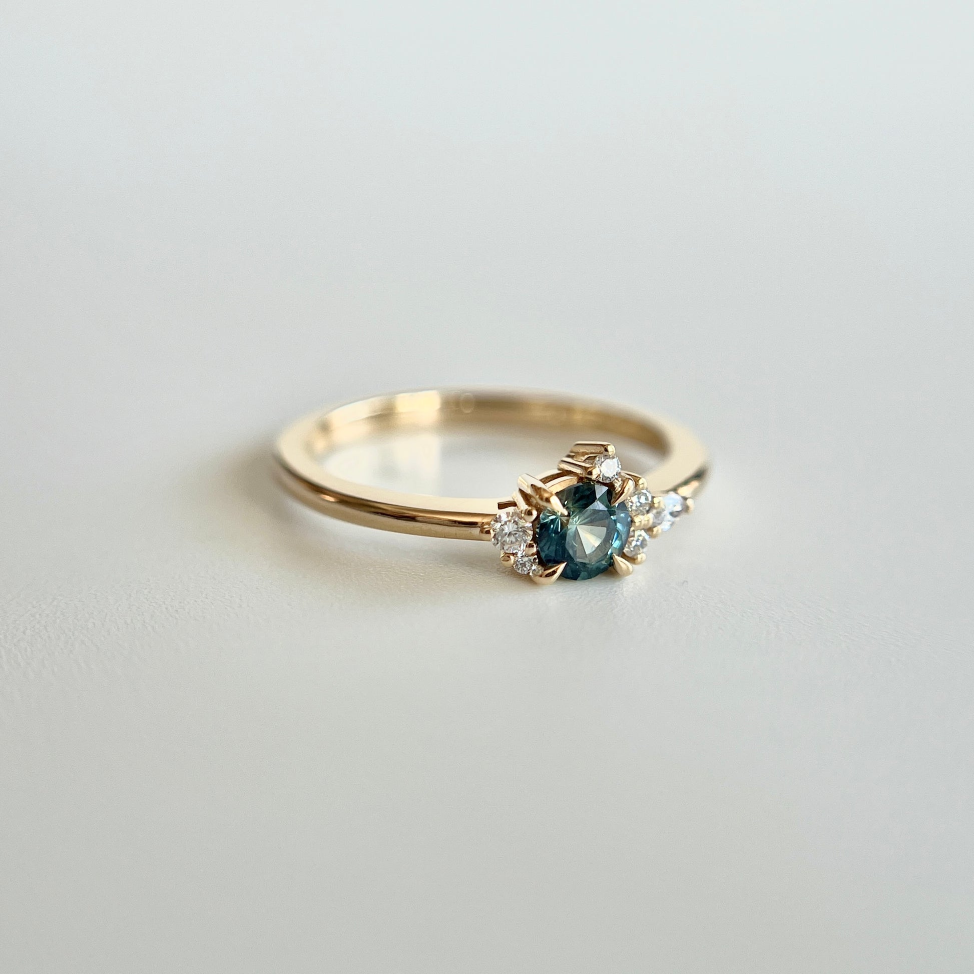 Bague de fiançailles en saphir sarcelle rond de 0,38ct et diamants naturels en or jaune 14k, vue en trois-quarts montrant la couleur de la pierre et le détail du cluster asymétrique