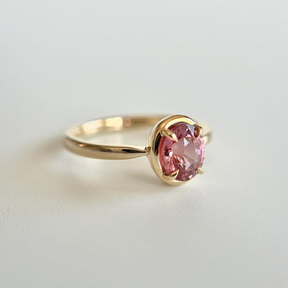 Bague de fiançailles solitaire en saphir ovale rose-orangé de 1,20ct en or jaune 14k, vue en angle montrant le détail du serti en griffes à cadre en or