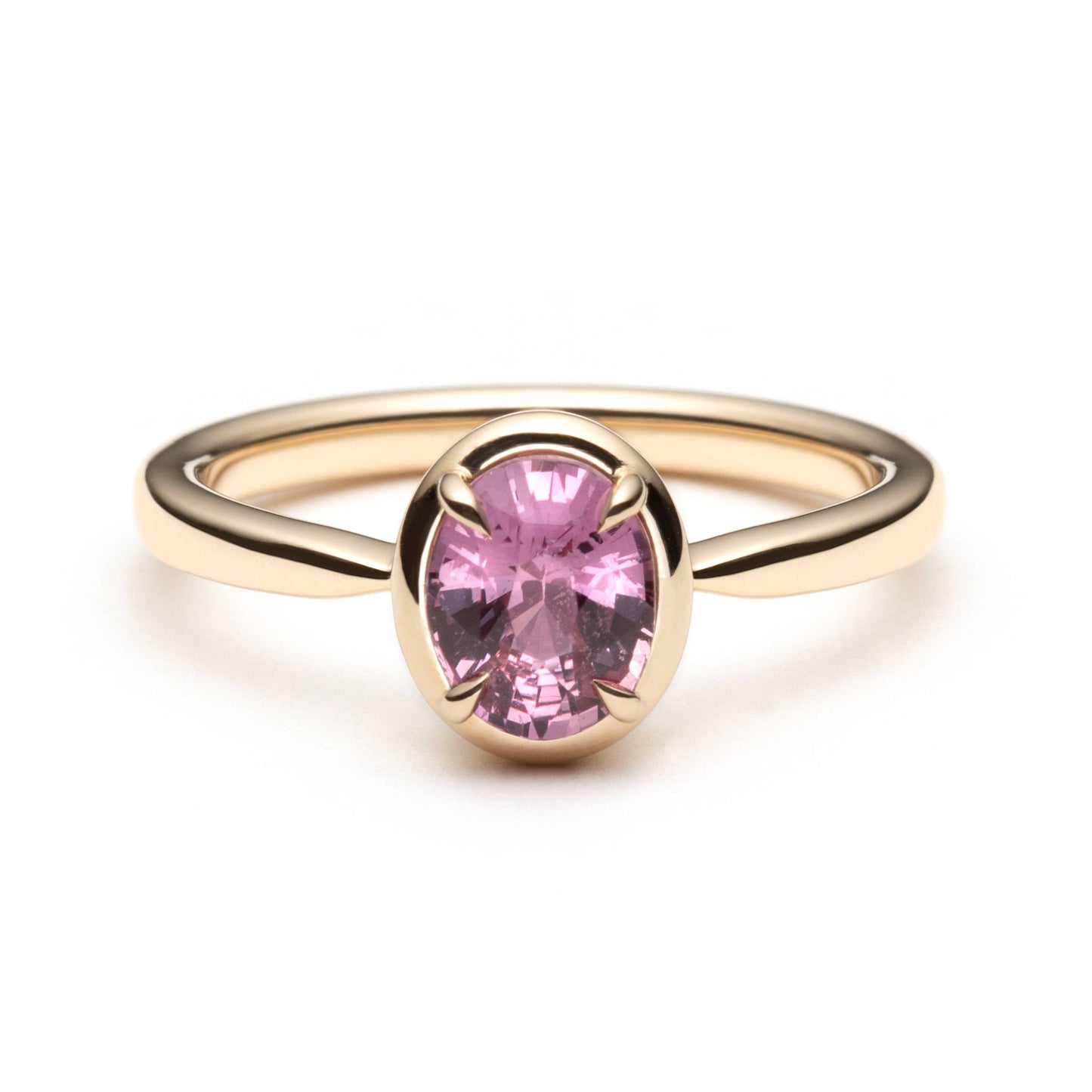 Bague de fiançailles solitaire en saphir ovale rose-orangé de 1,20ct en or jaune 14k avec serti en griffes à cadre en or, vue de face sur fond blanc montrant la couleur complète de la pierre
