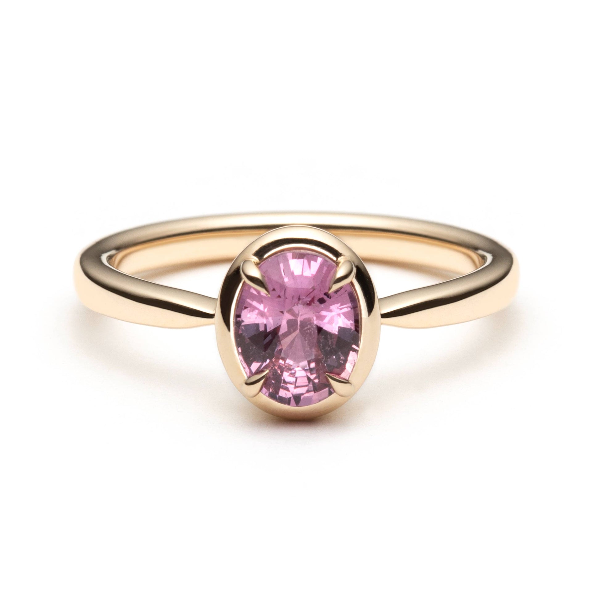 Bague de fiançailles solitaire en saphir ovale rose-orangé de 1,20ct en or jaune 14k avec serti en griffes à cadre en or, vue de face sur fond blanc montrant la couleur complète de la pierre
