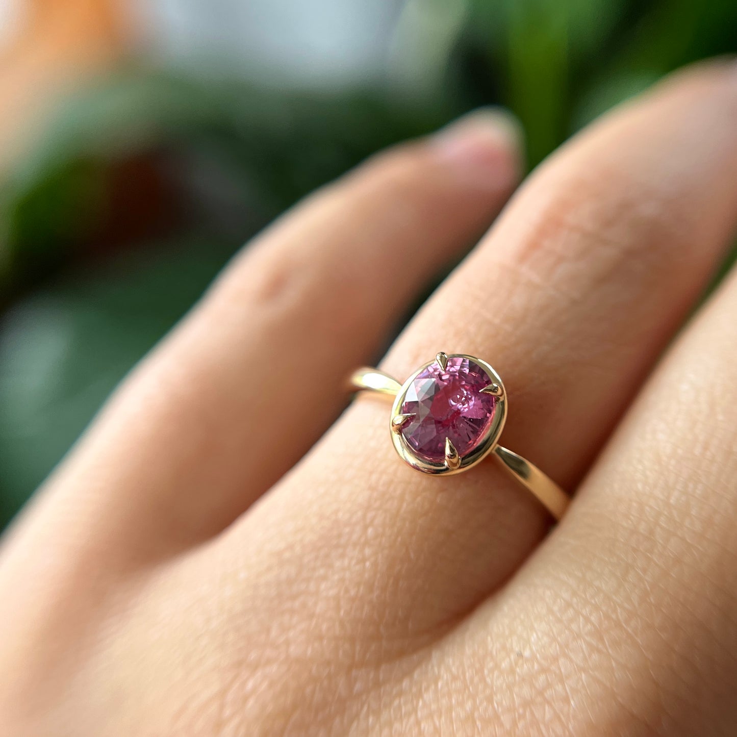 Bague de fiançailles solitaire en saphir ovale rose-orangé de 1,20ct en or jaune 14k avec serti en griffes à cadre en or, portée au doigt montrant la couleur de la pierre et le détail du serti