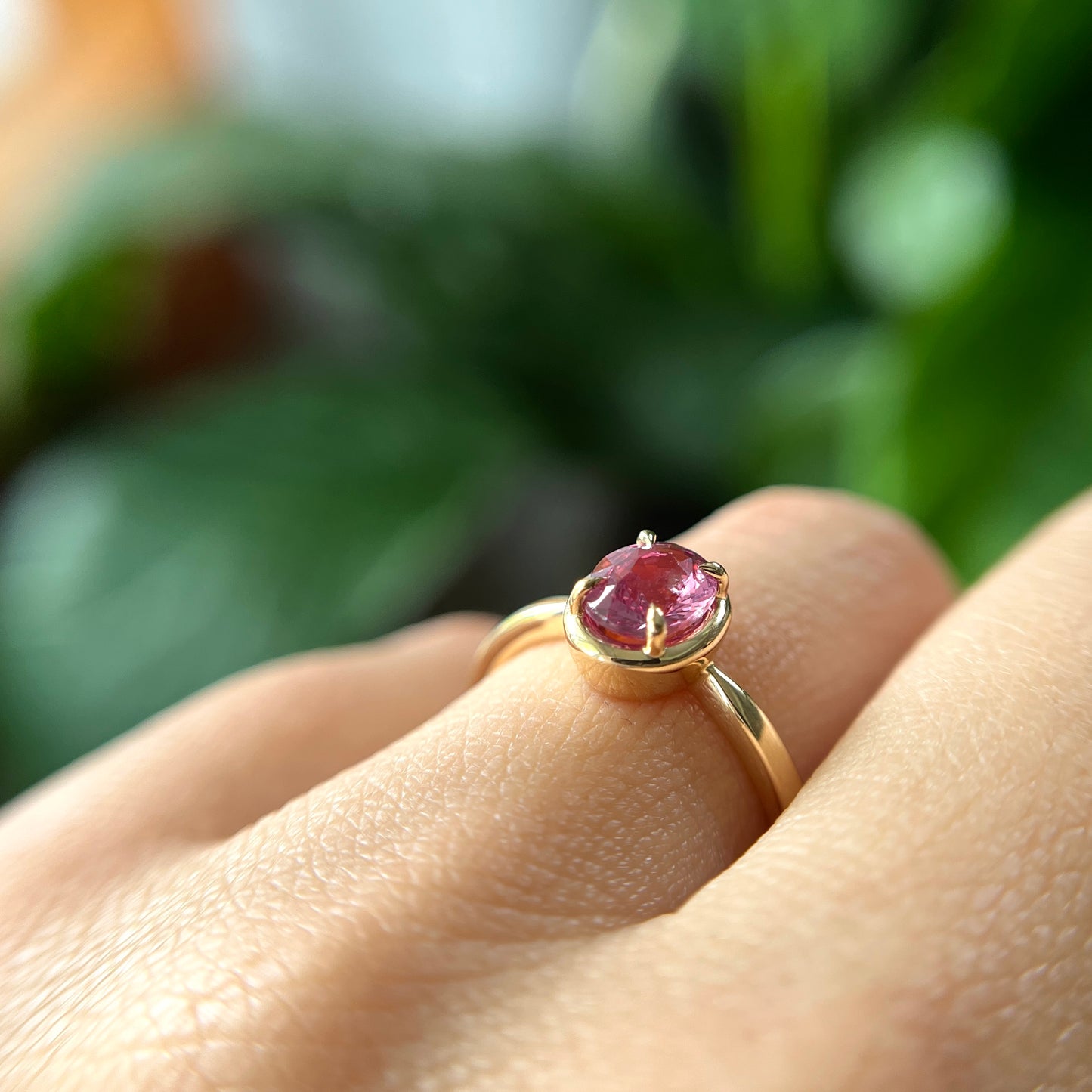 Bague de fiançailles solitaire en saphir ovale rose-orangé de 1,20ct en or jaune 14k, vue de côté portée au doigt montrant le profil du corps de bague et la hauteur du serti