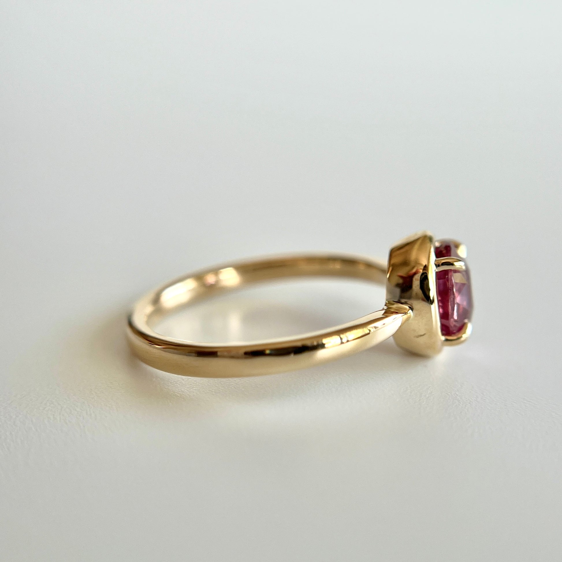 Bague de fiançailles solitaire en saphir ovale rose-orangé de 1,20ct en or jaune 14k, vue de côté montrant le profil du corps de bague et la hauteur du serti