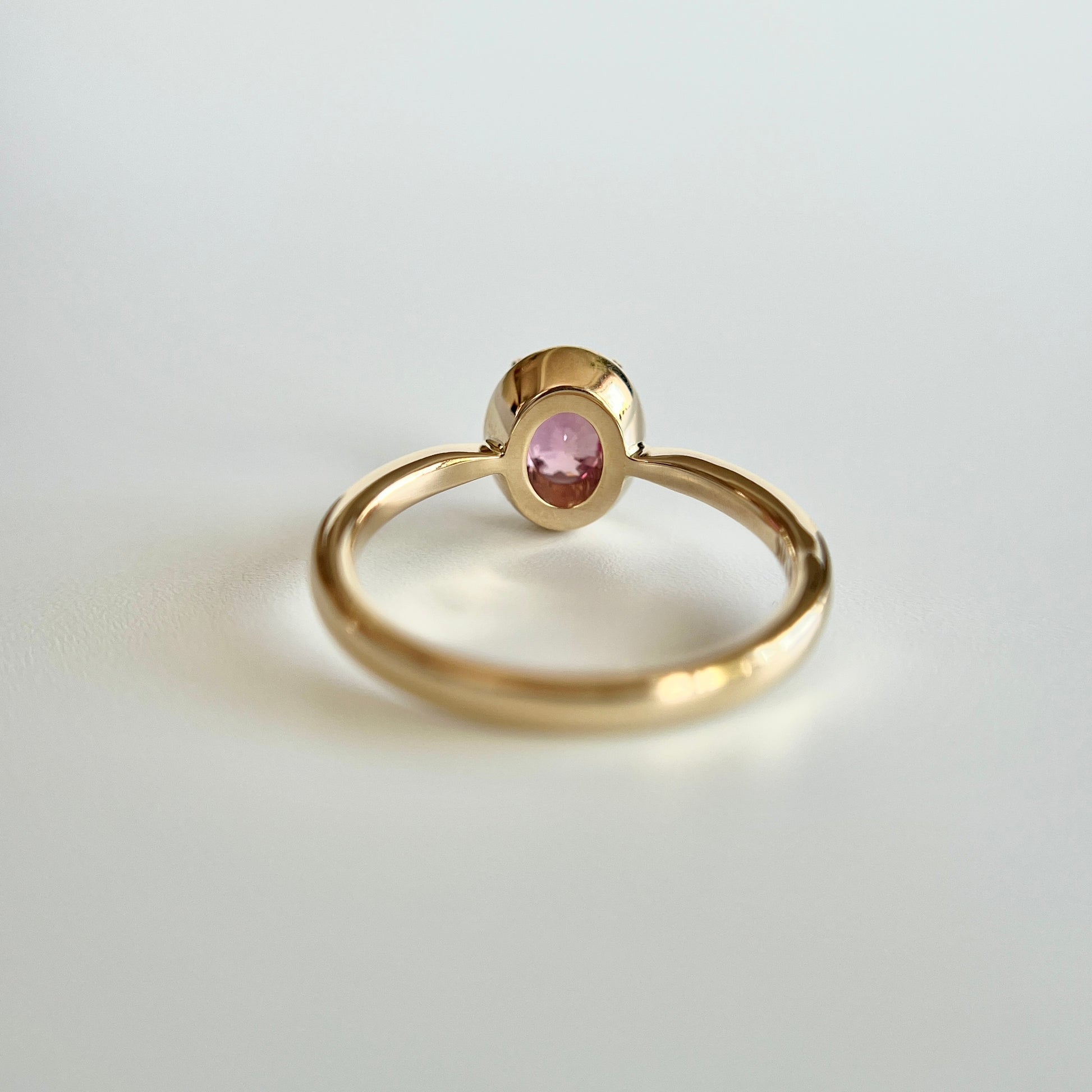 Bague de fiançailles solitaire en saphir ovale rose-orangé de 1,20ct en or jaune 14k, vue du dessous montrant la construction du serti et le détail du corps de bague