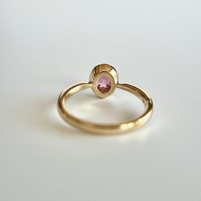 Bague de fiançailles solitaire en saphir ovale rose-orangé de 1,20ct en or jaune 14k, vue du dessous montrant la construction du serti et le détail du corps de bague