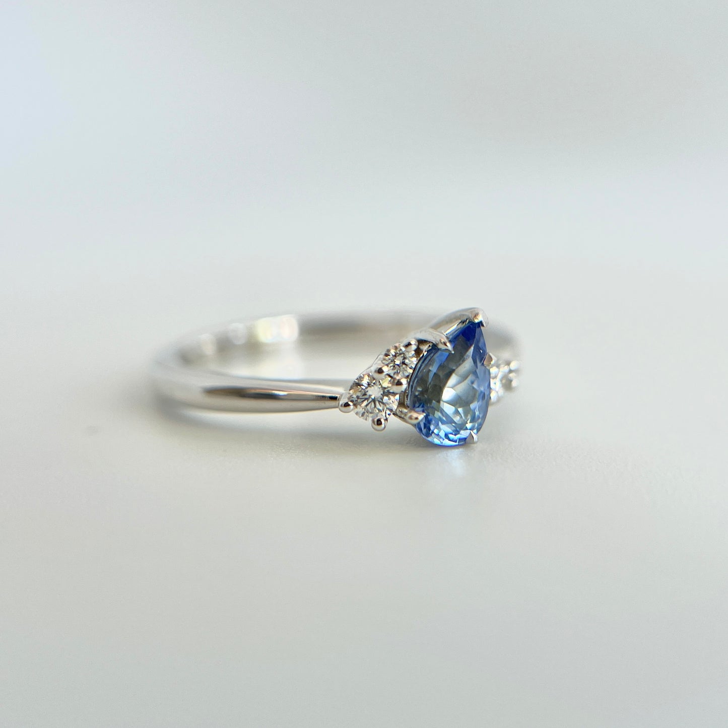 Bague de fiançailles en saphir bleu taille poire de 0,52ct du Sri Lanka et diamants naturels en or blanc 14k, vue en angle montrant la pierre inclinée et le détail du serti de diamants