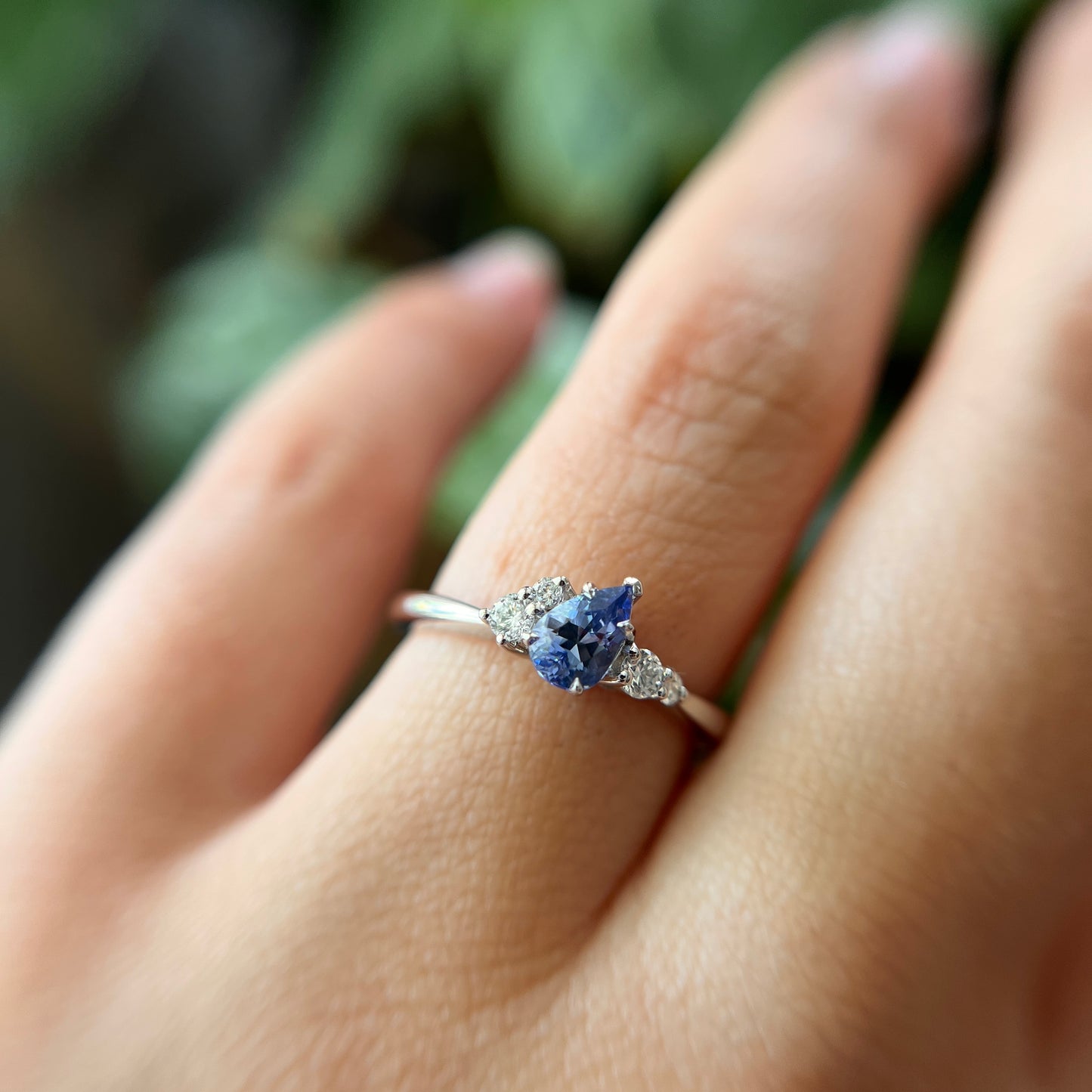Bague de fiançailles en saphir bleu taille poire de 0,52ct du Sri Lanka et diamants naturels en or blanc 14k, portée au doigt montrant la pierre inclinée et le serti asymétrique